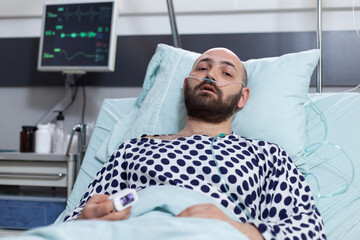 Obraz premium Portrait of patient with breathing problems recieving treatment connected to pulse oximeter and central line catheter lying in hospital bed. Man recovering after surgery treated with intravenous