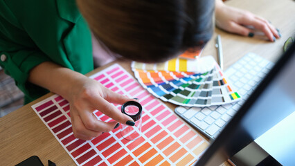 Designer looks through magnifying glass at samples of colors and shades of red on paper palette