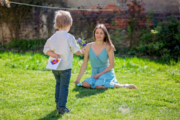 Beautiful kid and mom in spring park, flower and present. Mother getting gift from toddler boy for Mothers day