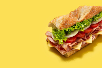 Submarine sandwich with ham, cheese, lettuce, tomatoes,onion, mortadella and sausage on yellow background. Copy space