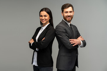 Concept of partnership in business. Young man and woman standing back-to-back with crossed hands against grey background