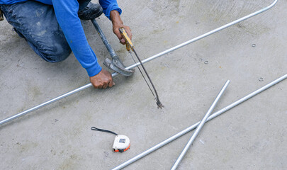 Builder worker using hacksaw to cutting conduit pipes on concrete floor for interior electrical installation work in construction site - obrazy, fototapety, plakaty