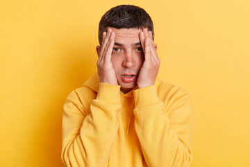 Sick man wearing casual style hoodie posing isolated over yellow background, frowning and clasping...