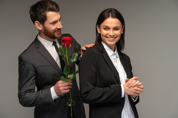 Young man giving red rose to his girlfriend on grey background. Romantic couples and love concept. Stock photo