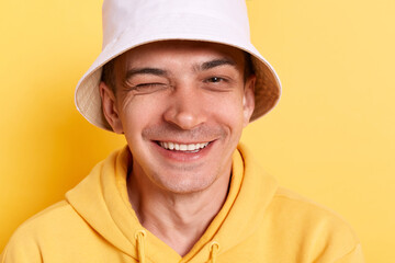 Indoor shot of childish man wearing casual style hoodie and panama posing isolated over yellow...