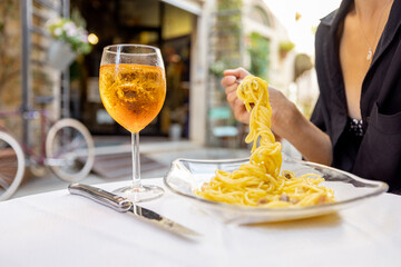 Young woman having lunch with pasta and wine at cozy italian restaurant outdoors. Concept of...
