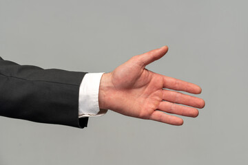 Cropped view of the male businessman in a suit stretching hand and shows a palm up gesture on a grey background. Concept of request, handshake