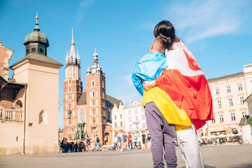 woman and little boy covered with ukraine and poland flag in city center
