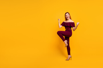 Fototapeta na wymiar Full length photo of excited charming young lady dressed red clothes walking empty space rising fists isolated yellow color background