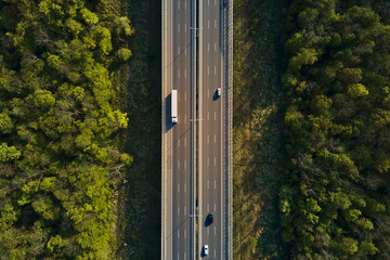 Car traffic moving on highway, aerial view. Countryside road through forest. Road trip, delivery and logistic concept