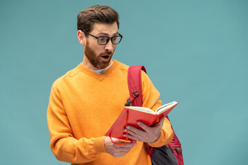 Astonished smart bearded student man lowered my glasses while reading book with surprised...