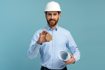 Architect man with smiled face in builder safety helmet looking at the camera and holding house...