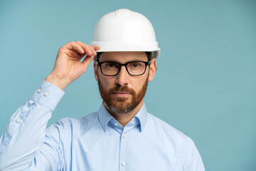 Architect man with serious face in builder safety helmet looking at the camera through his glasses over isolated background. Engineer concept