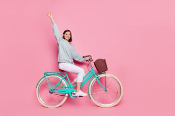 Full size profile side photo of young girl wave hi ride bicycle weekend isolated over pink color...