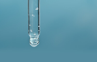 Closeup of pipette with serum, hyaluronic acid on blue background. Cosmetics and healthcare concept. Dose of essential oill, retinol with air bubbles. Beauty product presentation, front view, macro