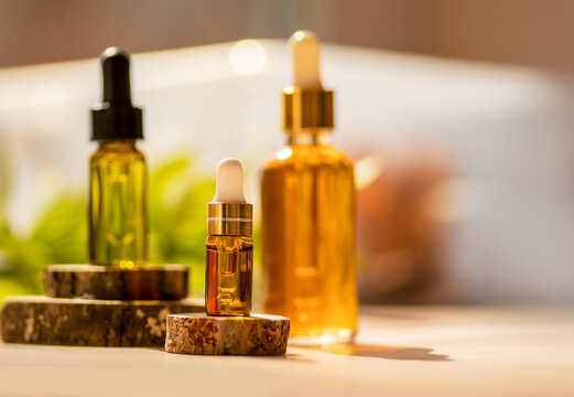 Cosmetic glass dropper bottles on wooden podium with oil, serum, fruit peeling in the sunlight. Soft focus. Natural beauty products background. Morning routine, skin care concept. Front view, mockup