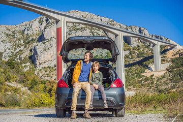 Montenegro. Dad and son tourists are sitting on the trunk of a car. Road trip around Montenegro. Bridge Moracica. Reinforced concrete bridge across the Moraci gorge. The motorway Bar - Bolyare. The