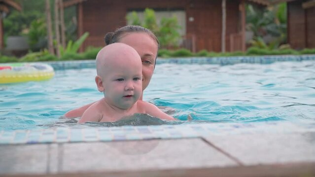 Kid learning to swim. Mom is engaged in the pool with a child
