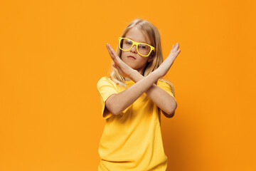 a serious, stern girl of school age stands on a yellow background and shows a prohibition sign with her hands