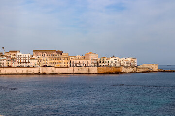Fototapeta na wymiar Panoramic view on the waterfront of the city of Syracuse, Sicily, Italy, Europe EU. Soft light shining on the residential houses at the Mediterranean seaside. Walking along the coastline