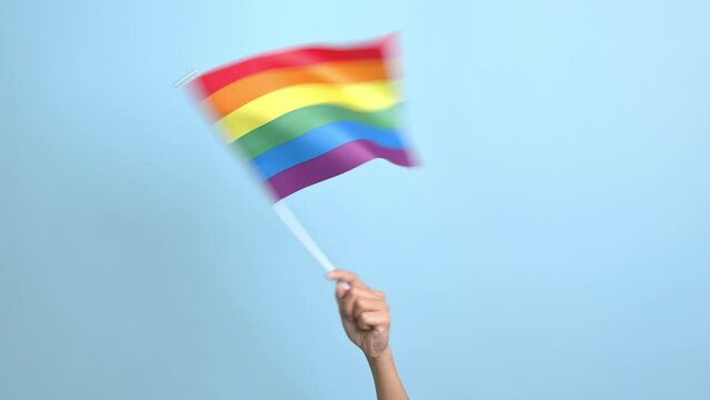 LGBT gay pride rainbow flag being waved at a pride march celebration event on blue background.