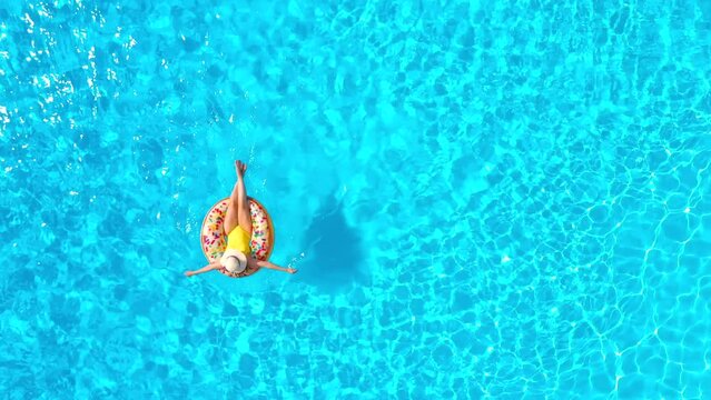Aerial view of a woman in yellow swimsuit lying on a donut in the pool