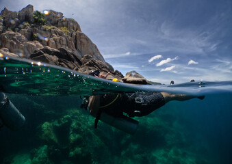 Scuba diver in tropical waters half way under water - half view of underwater view and sky and rocks above