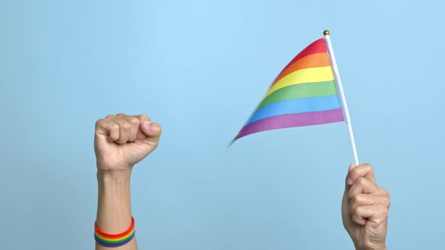 lgbt gay pride rainbow colored male hand raising up with fist in protest on blue background.