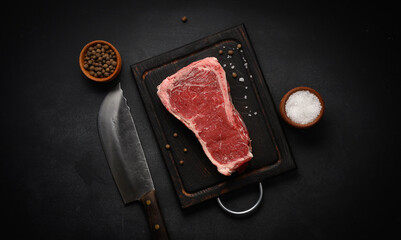 Fresh raw piece of beef meat, striploin steak on a black background, top view. Marbled piece of meat New York
