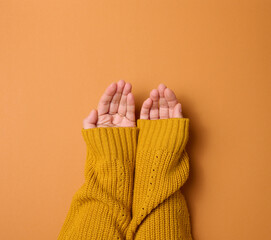 two female hands folded palm to palm on an orange background, top view