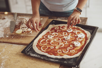 A woman lays out the ingredients on the pizza before baking. Pizza at home