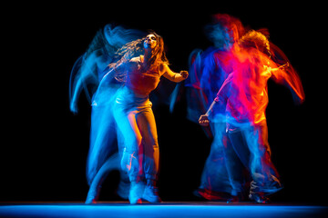 Excited man and woman dancing hip-hop in sportive style clothes on dark background at dance hall in mixed neon light. Youth culture, hip-hop, movement