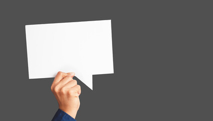 Close-up of hand holding a white speech bubble against a gray background