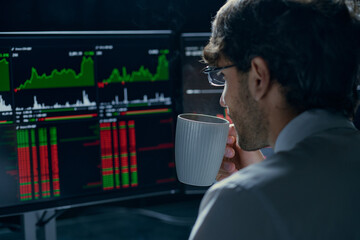 young trader with a cup of coffee is following the data of the cryptocurrency market.
