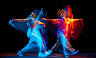 Fototapeta na wymiar Dance show. Flexible man and girl, hip-hop dancers in motion and action isolated on dark background at dance hall in blue mixed neon light. Youth culture, hip-hop, movement