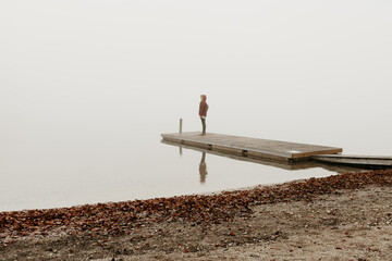 A woman is standing on a wooden pier at lake Bohinj in Slovenia. She is facing the distance. The...