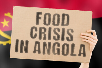 The phrase " Food crisis in Angola " is on a banner in men's hands with a blurred Angolan flag in the background. Crisis. Finance. Life. Nutrition. Bread. Disaster. Collapse. Social issue. Problem