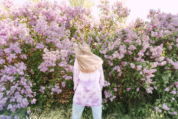 Young blond woman dance among lilac flowers back view no face
