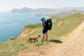 Young beautiful woman in hood travel with her dog and backpack on mountains road