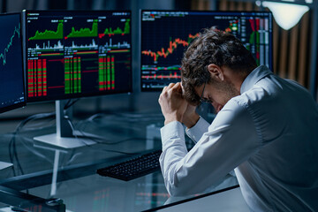 worried young investor sitting at a computer desk . - 506834548