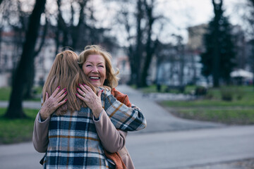 Grandmother and adolescent granddaughter are hugging during the walk on the street in cold weather.