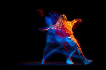 Young woman dancing hip-hop in sportive style clothes isolated on dark background at dance hall in...