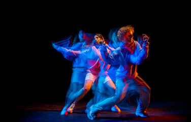 Dance show. Flexible man and girl, hip-hop dancers in motion and action isolated on dark background at dance hall in blue mixed neon light. Youth culture, hip-hop, movement