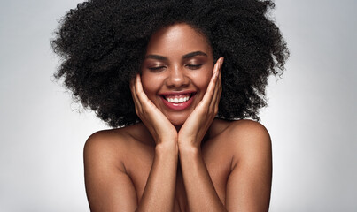 Happy ethnic lady smiling and touching face during skin care procedure