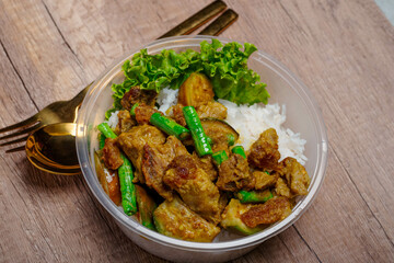 Fried crispy pork with green curry paste and vegetables in plastic cups on wooden floor