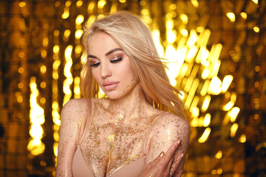 Glowing gold skin. Fashion blonde model woman face in bright golden glitter. Beautiful sexy woman portrait with white hair and trendy make-up. Glittering, golden, shine makeup.