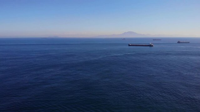 Large bulk carrier sails from Algeciras in the Strait of Gibraltar while passing another freighter en route to the Atlantic with in the background the coast of Africa and anchored ships. Drone lifting