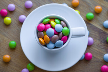 Fototapeta na wymiar Colorful multi-colored dragees in a white cup. Small colorful candies. Colorful chocolate dragee. Selective focus.