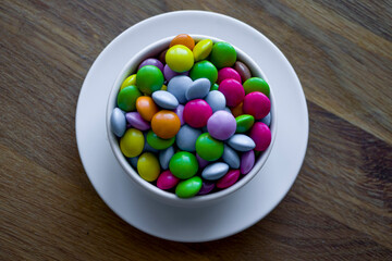 Colorful multi-colored dragees in a white cup. Small colorful candies. Colorful chocolate dragee.