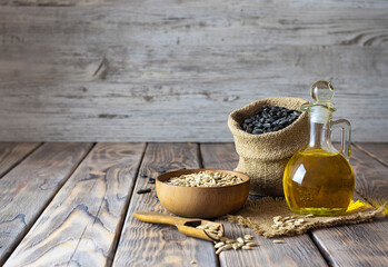 Jug with golden sunflower oil on a canvas napkin. Sunflower seeds in a canvas bag in the background. Peeled seeds on the table. Light wooden background, space for text